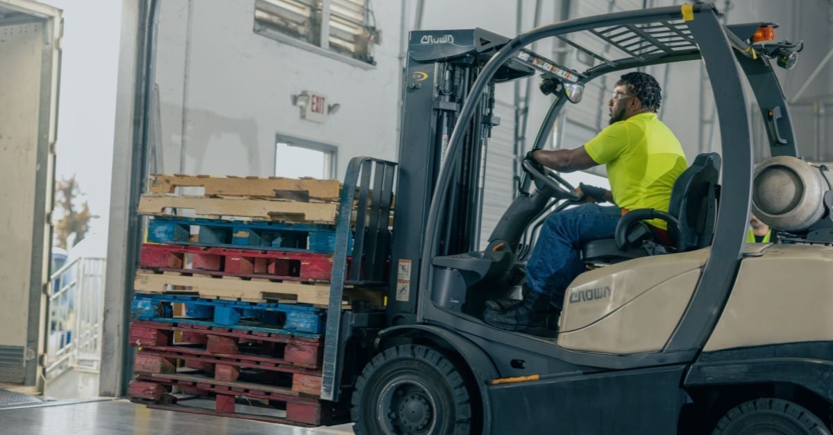 Forklift operator unloading colorful wooden pallets at a distribution center, enhancing logistics efficiency for grocery supply chain operations.