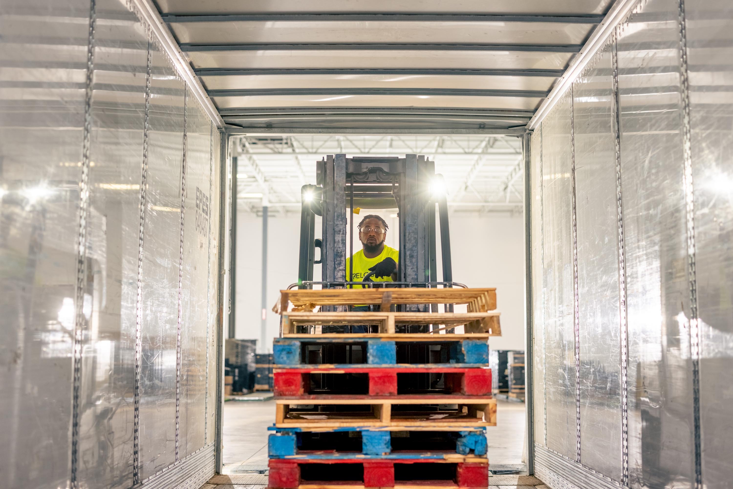 Forklift operator inside a trailer, maneuvering stacked wooden pallets, emphasizing supply chain efficiency and pallet management at Relogistics.