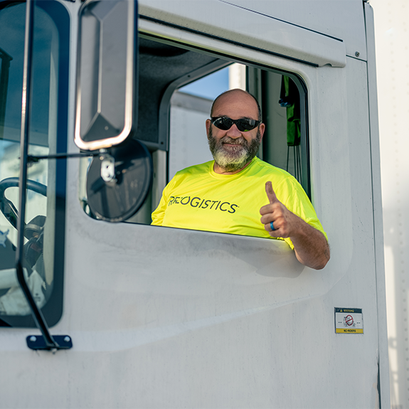 Driver in bright yellow Relogistics shirt giving a thumbs up from truck window, representing efficient supply chain management and customer service.