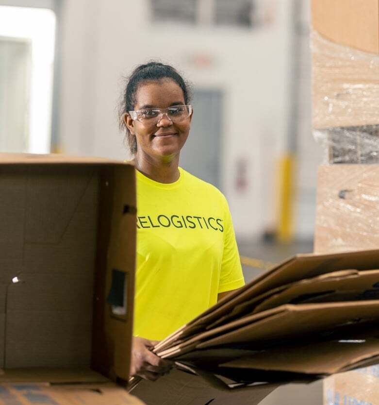 Worker in bright yellow Relogistics shirt managing cardboard boxes in a logistics facility, emphasizing supply chain efficiency and operational support.