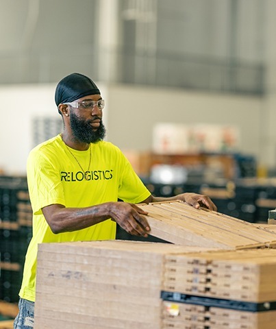 Worker in bright yellow Relogistics shirt handling pallets in a warehouse, emphasizing labor management solutions and supply chain efficiency.