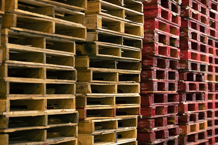 Stacks of wooden pallets in various colors, showcasing pallet management solutions relevant to supply chain efficiency in the food service industry.