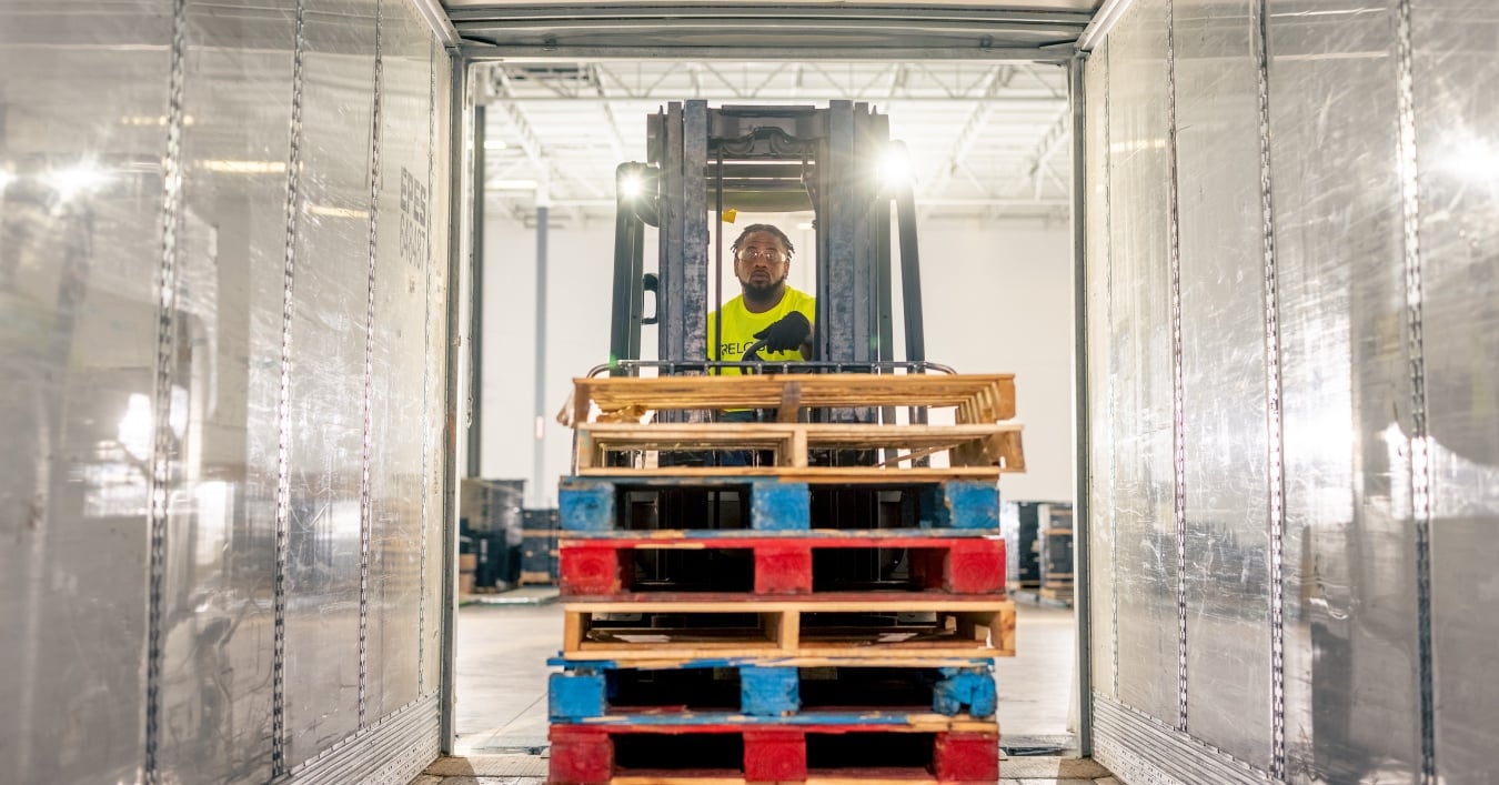 Forklift operator maneuvering mixed pallets in a warehouse, showcasing pooled pallet management for supply chain efficiency.