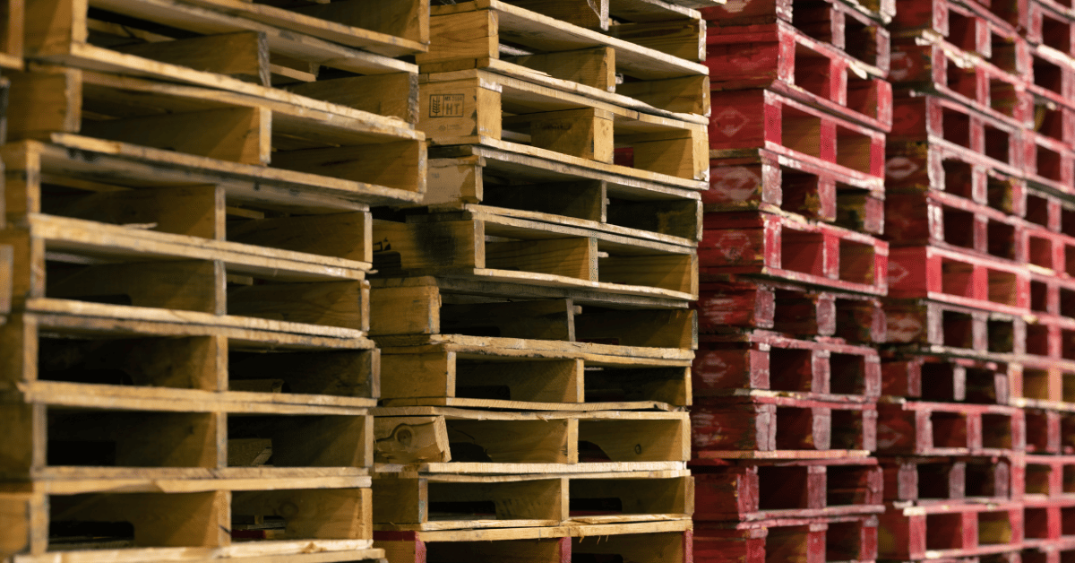 Wooden pallets stacked in a warehouse, featuring a mix of natural and red-painted pallets, illustrating essential pallet types for e-commerce supply chain management.