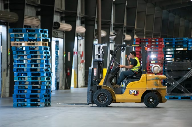 Forklift operator managing blue pooled pallets in a logistics facility, illustrating efficient pallet management solutions for retail supply chains.