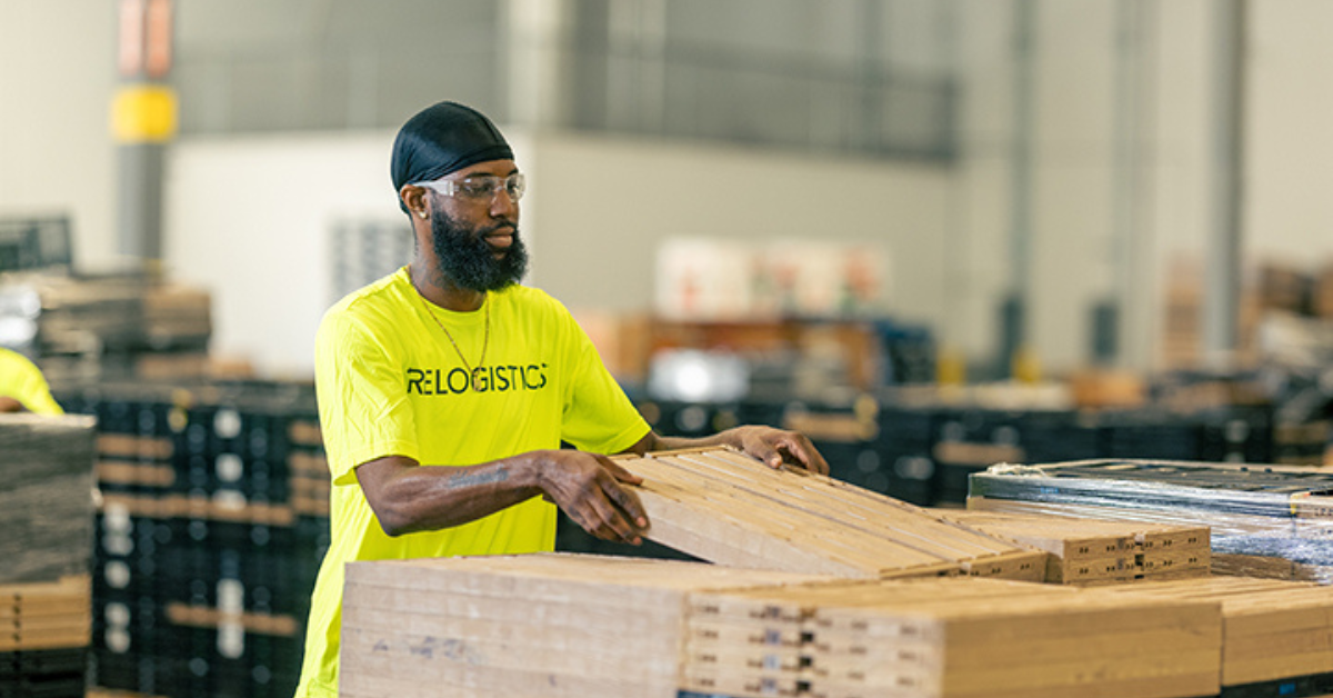 Worker in yellow Relogistics shirt handling pallets in a warehouse, emphasizing efficient pallet management for supply chain solutions in the food service industry.