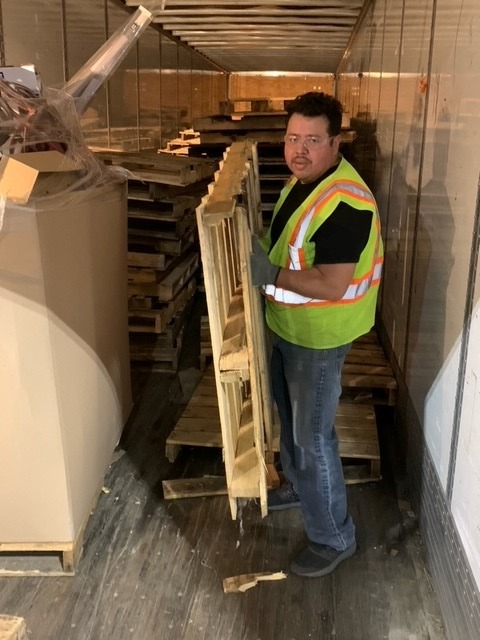 Supervisor Uciel Rodriguez wearing a safety vest and gloves, handling wooden pallets in a logistics trailer, emphasizing dedication to safety and compliance in operations.