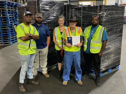 RPC sorter William Sanders with team members at Relogistics, celebrating safety achievements in front of stacked pallets, emphasizing the company's commitment to a culture of safety and employee recognition.