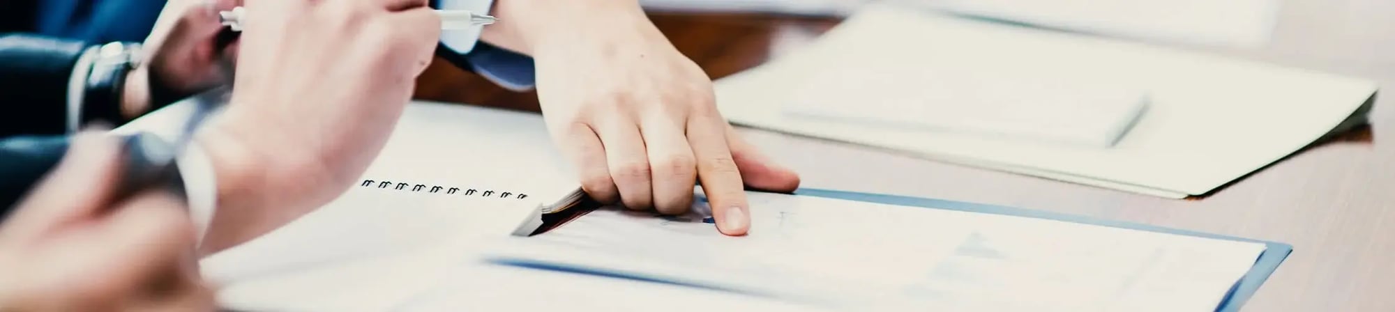 Hands pointing at a document on a table, emphasizing collaboration and data analysis in logistics reporting and optimization.