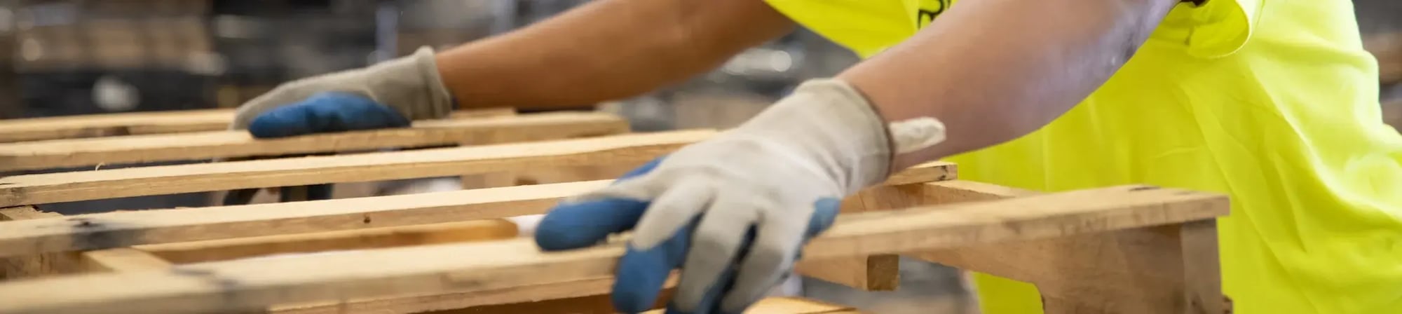 Worker inspecting and repairing wooden pallets, emphasizing the pallet repair process for sustainability and cost-effectiveness in supply chain management. Worker inspecting and repairing wooden pallets, emphasizing the pallet repair process for sustainability and cost-effectiveness in supply chain management.