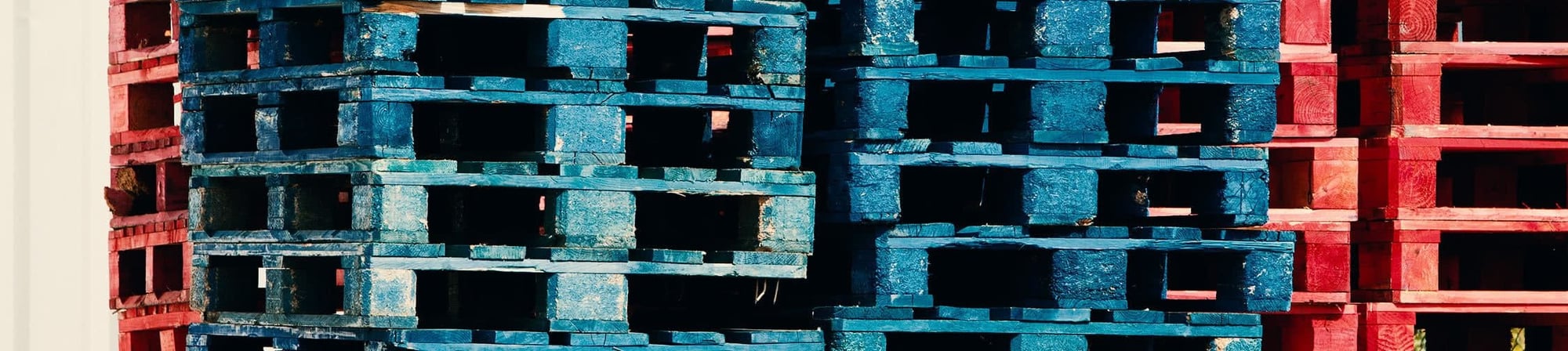 Stacks of blue and red wooden pallets, illustrating Relogistics' pallet sorting and handling solutions for supply chain efficiency. Stacks of blue and red wooden pallets, illustrating Relogistics' pallet sorting and handling solutions for supply chain efficiency.