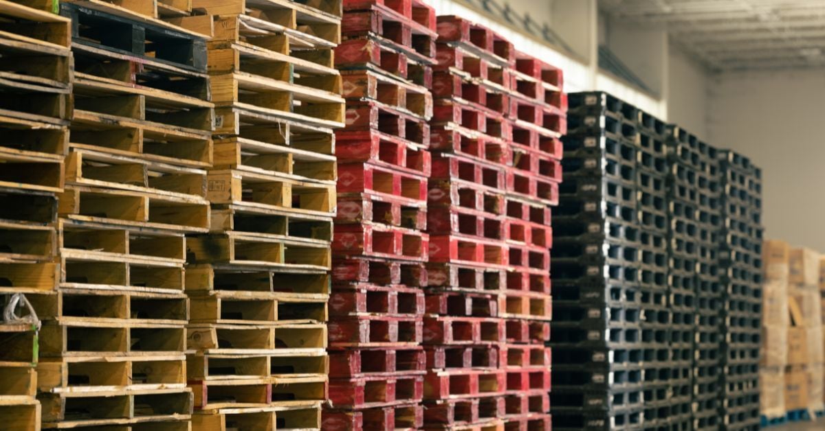 Stacks of wooden pallets in various colors, including red and black, arranged in a distribution center, illustrating pallet management solutions relevant to e-commerce fulfillment operations.