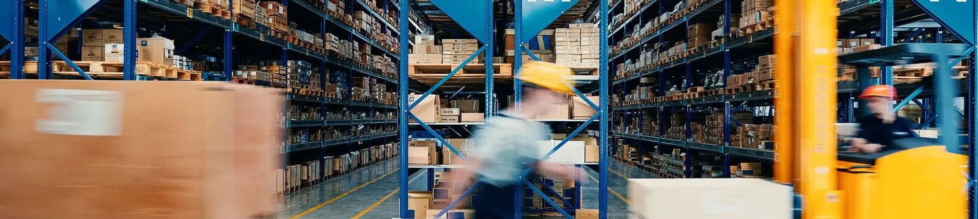 Warehouse workers moving quickly among shelves filled with pallets and boxes, emphasizing the importance of safety and efficiency in logistics operations.