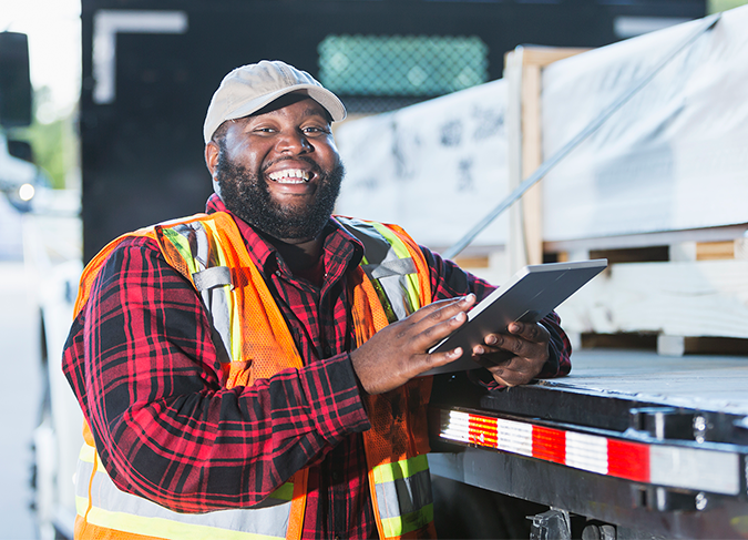 african american man looking at tablet with semi truck in background