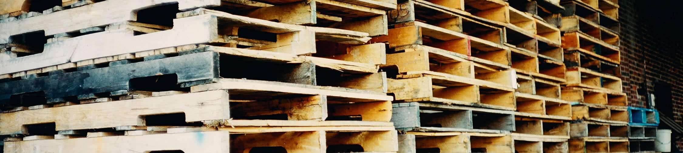 Stacked wooden pallets in a warehouse setting, illustrating efficient pallet management and logistics solutions related to custom pallet programs.